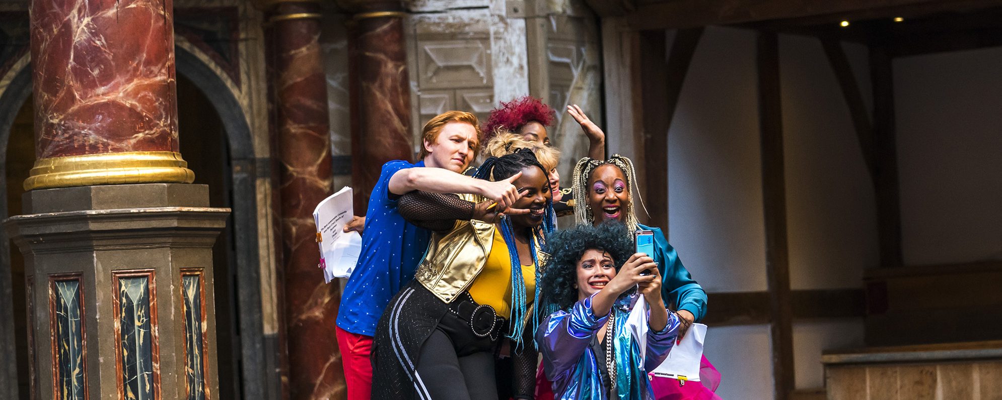 A group of actors huddle together to smile for a selfie on stage