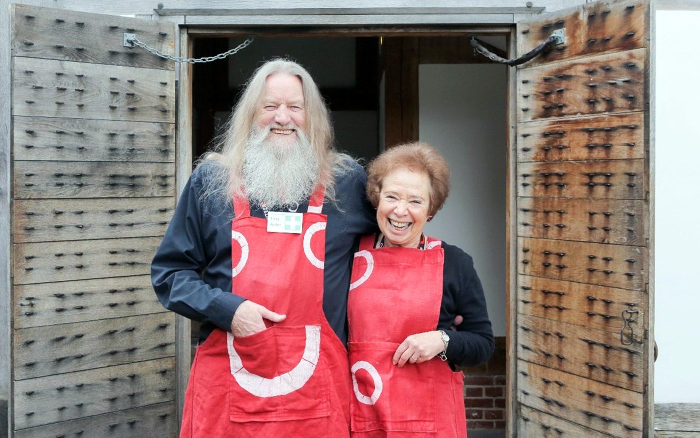 Two Globe Volunteers standing outside the East Tower entrance, wearing red Globe-brand aprons.