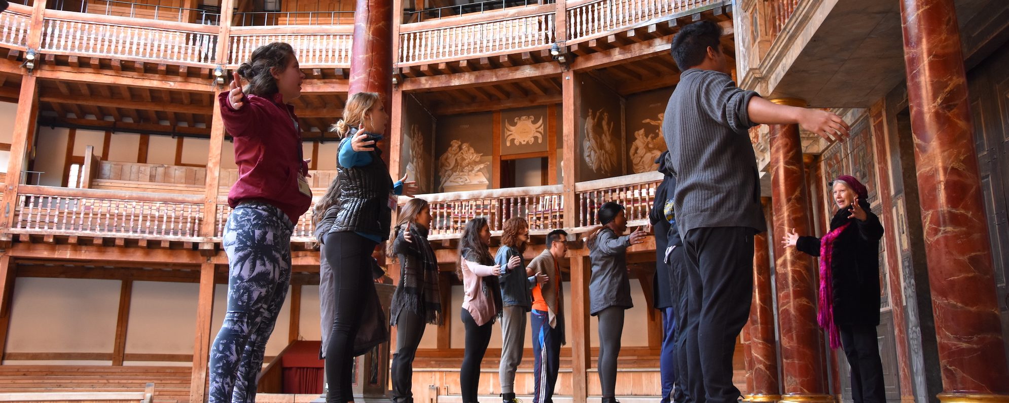 People stand on stage with their arms held out during a corporate workshop at Shakespeare's Globe