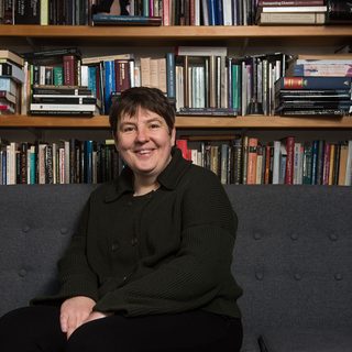 A person sits on a sofa in front of a bookshelf