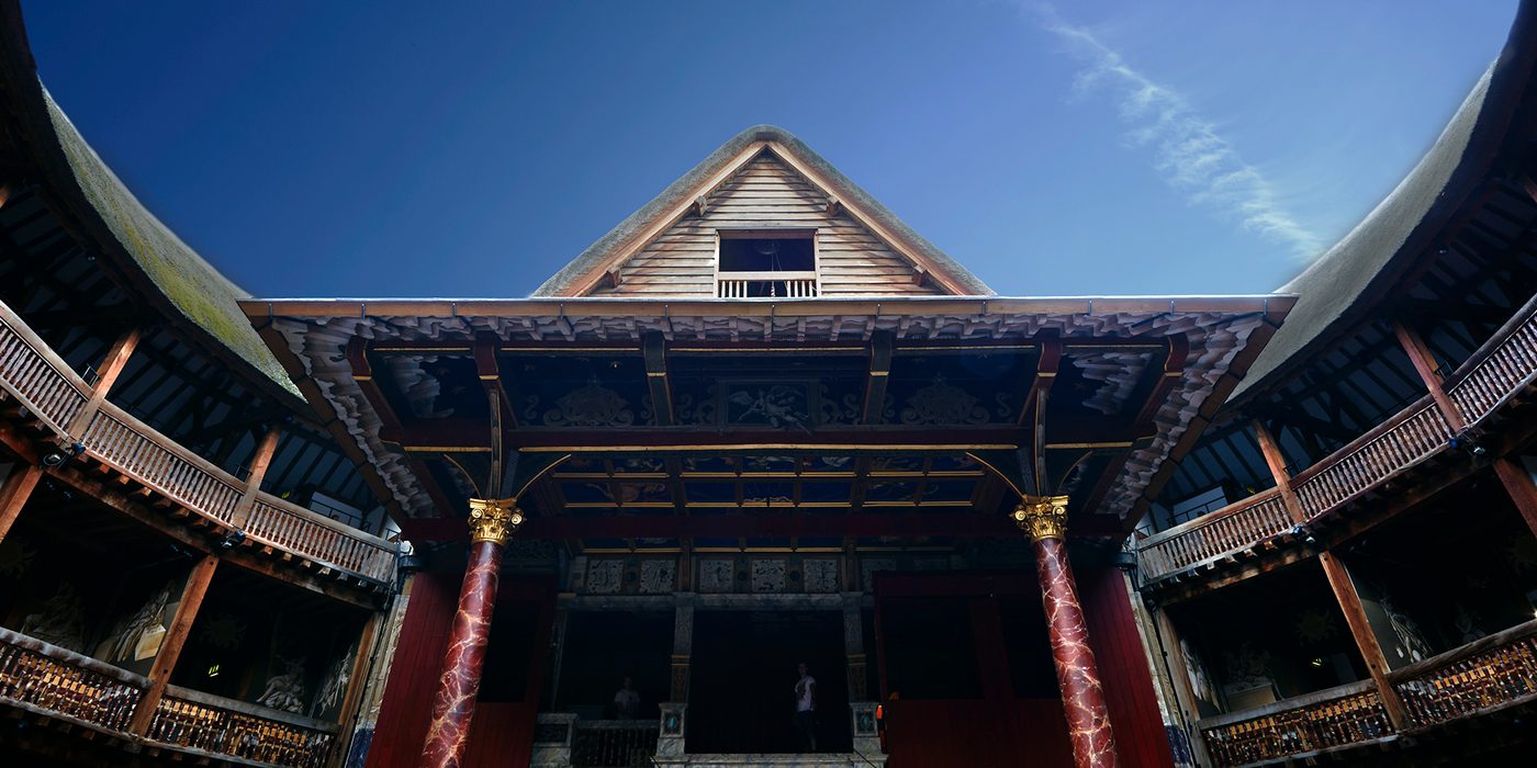 A blue sky over the pointed roof of a timber structure theatre.