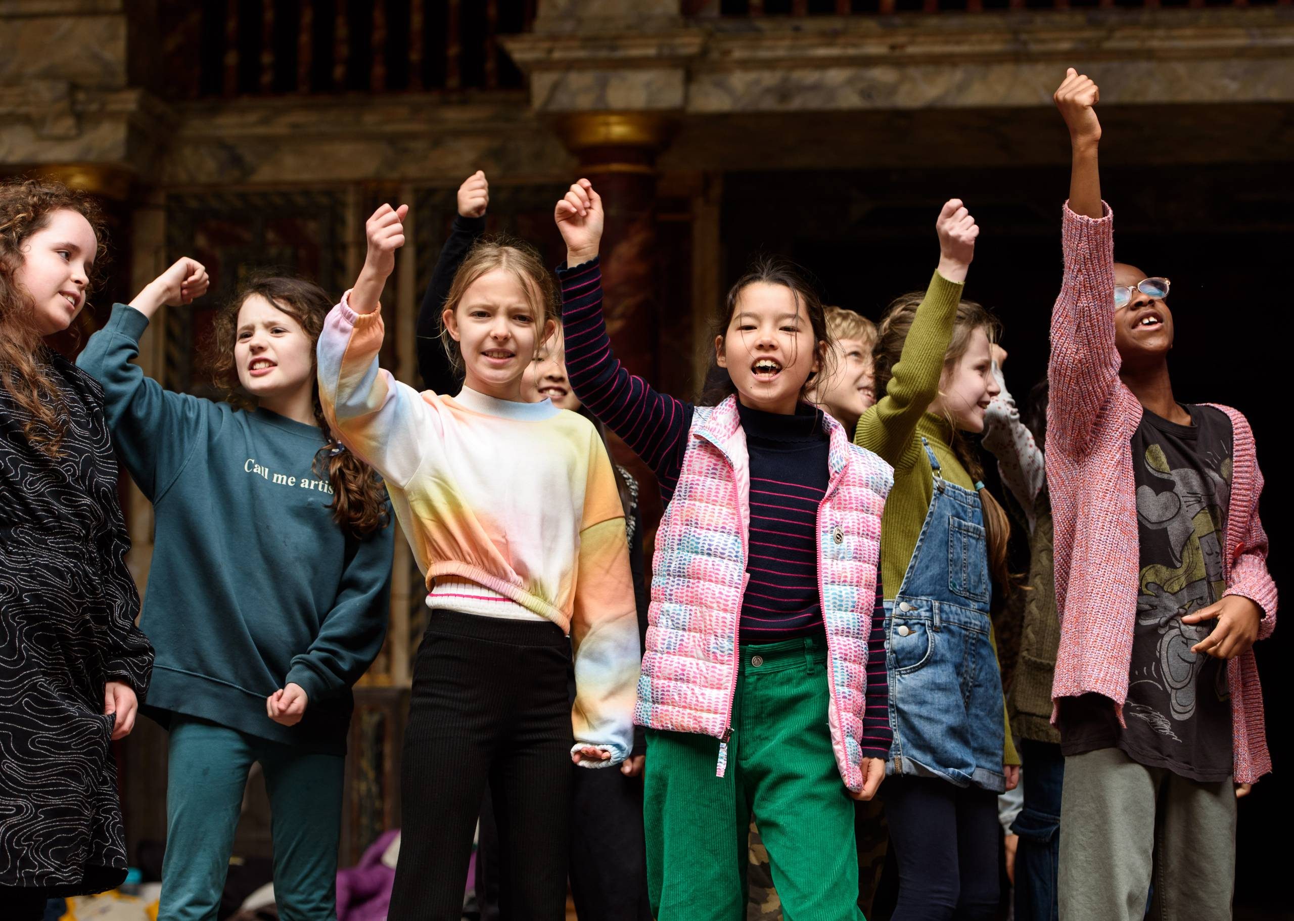 A group of young actors on stage, raising their fists to the sky