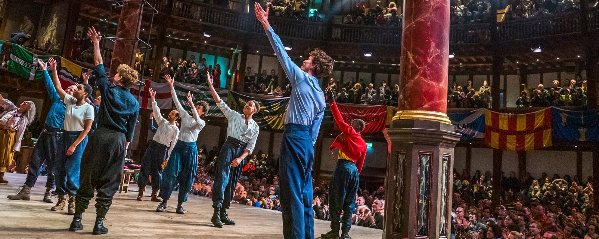 Actors on stage raise their arms to the sky in sync