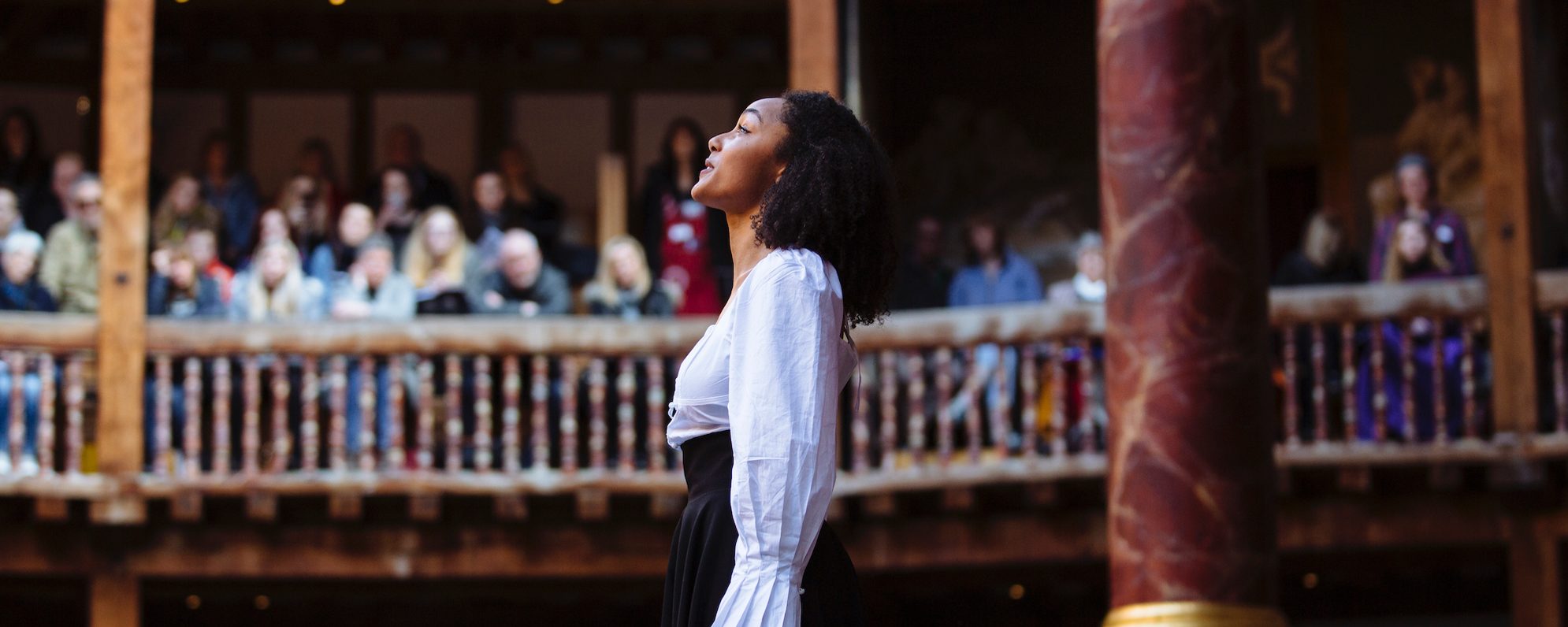 An actress stands on stage looking up to the sky