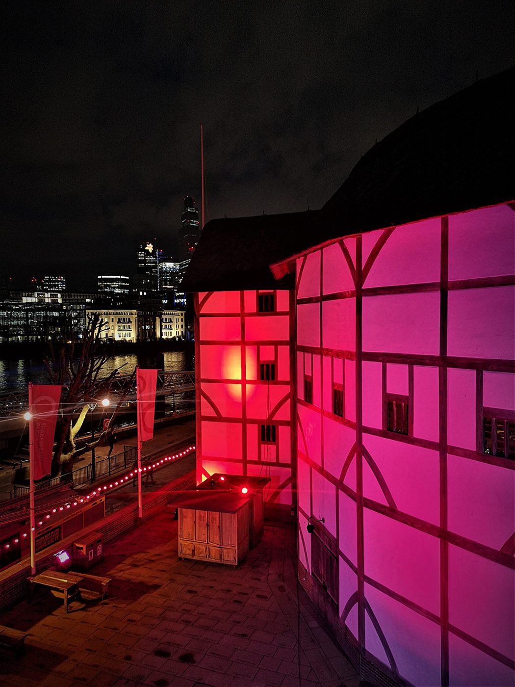 The normal white walls of the Globe Theatre are lit by red light.