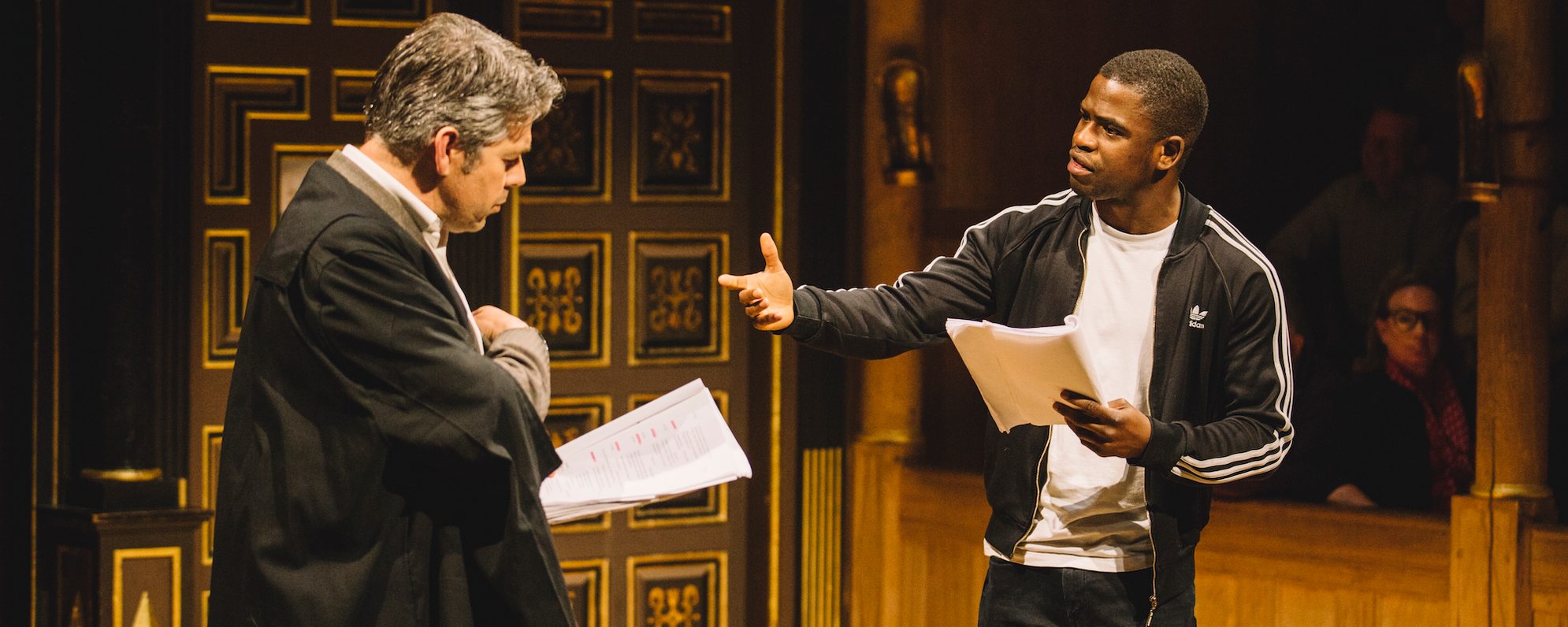 Two actors perform on stage with scripts