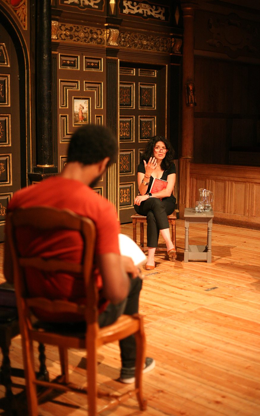 A woman talks to a group onstage as they sit on chairs