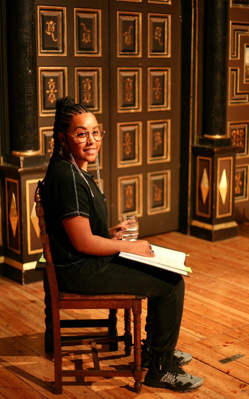 An actor wearing glasses sits on a chair