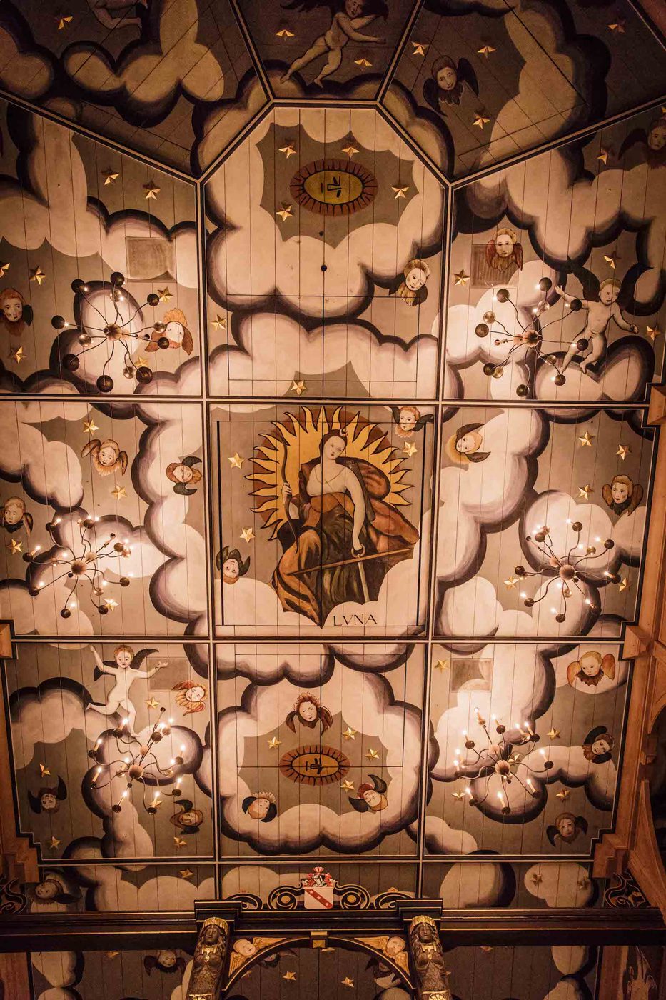 An intricately painted ceiling, looking up at it from below, with illustrations of clouds and angels