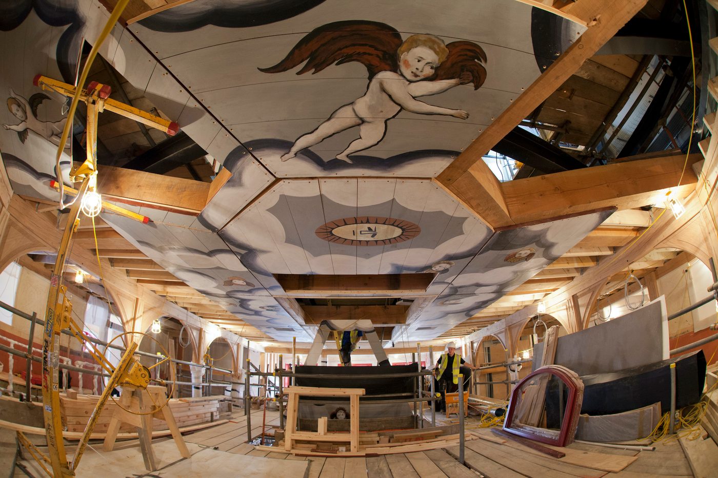 People work on building scaffolding which reaches a decorated ceiling