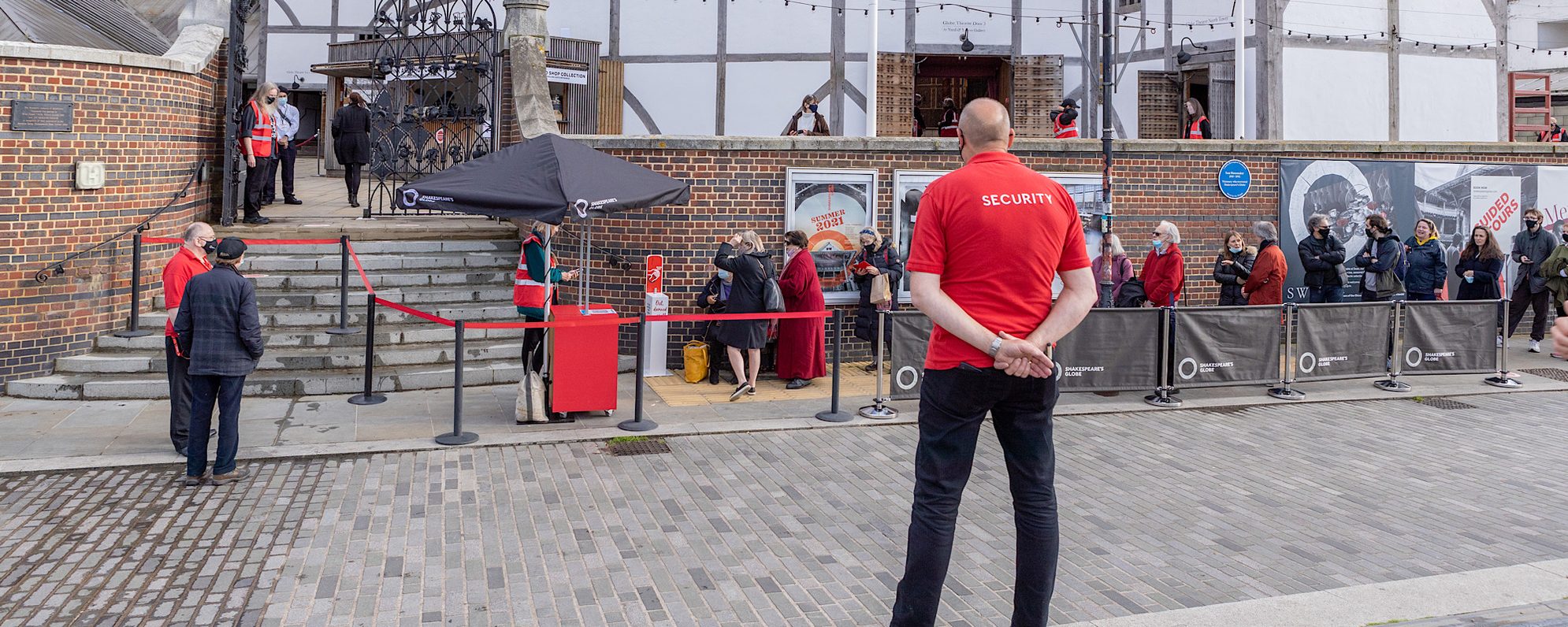 A person with a red shirt that has the words ‘security’ written on the back of it stands in front of an outdoor white theatre