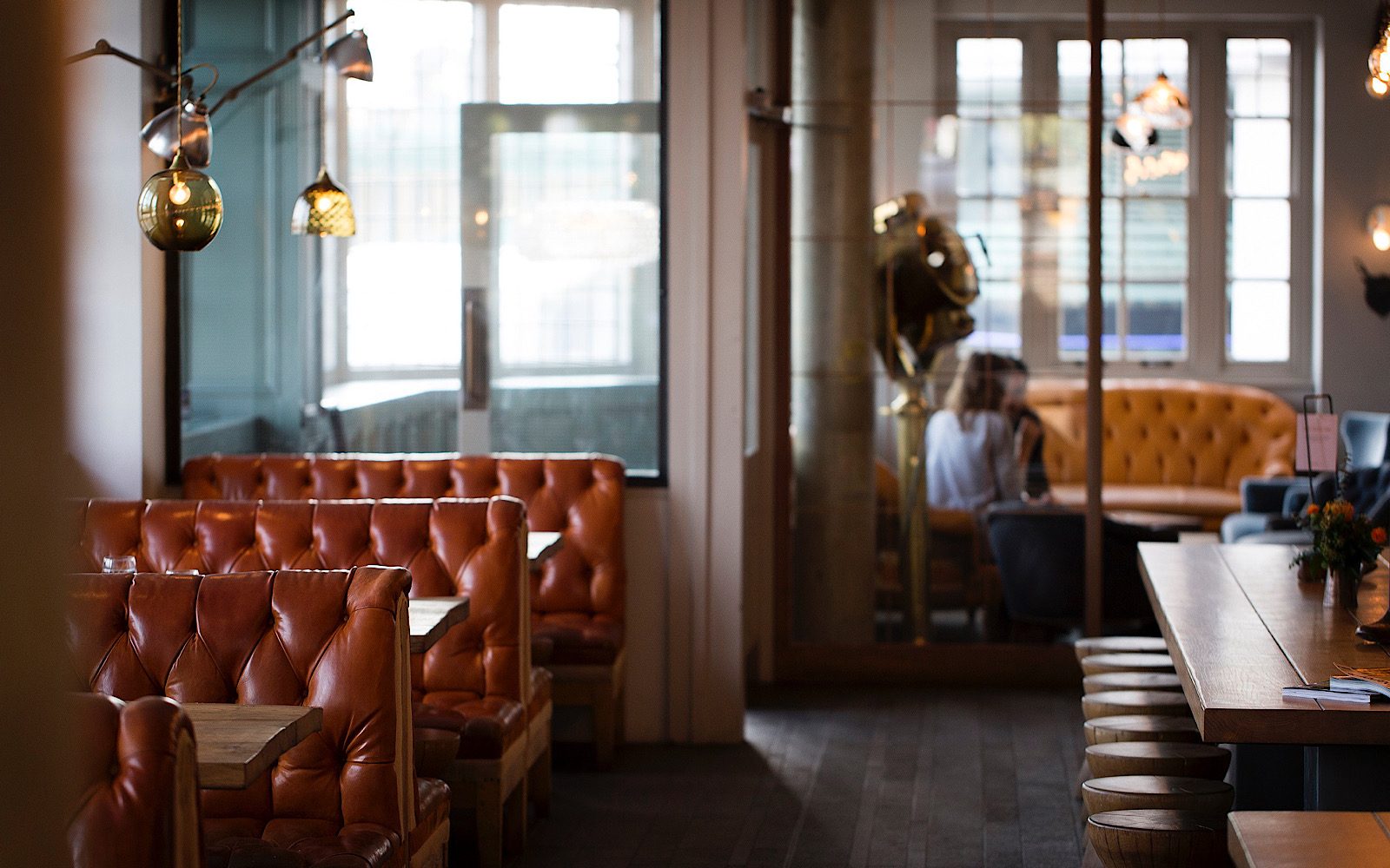 A quiet bar has booth seating to the side and a large bench to the other side, with people sitting in a booth in the far background