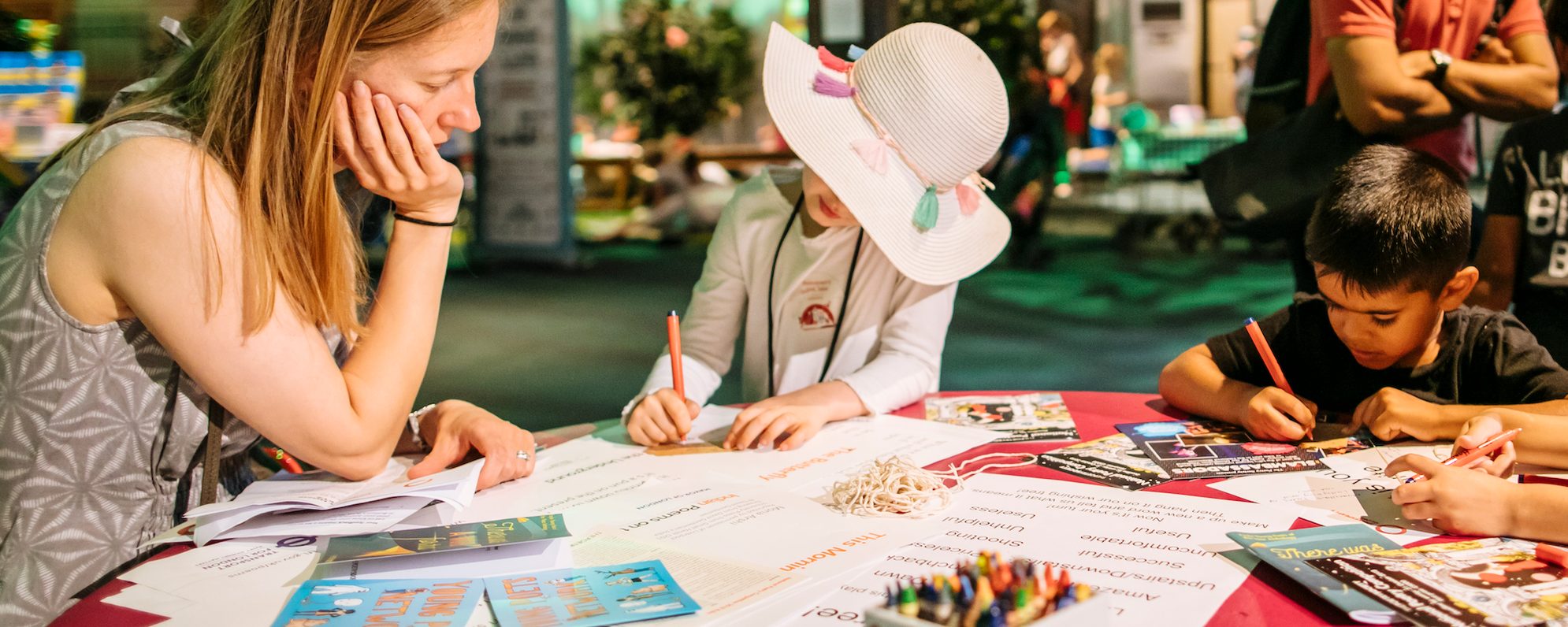 A woman oversees the work of two young children who are writing on paper