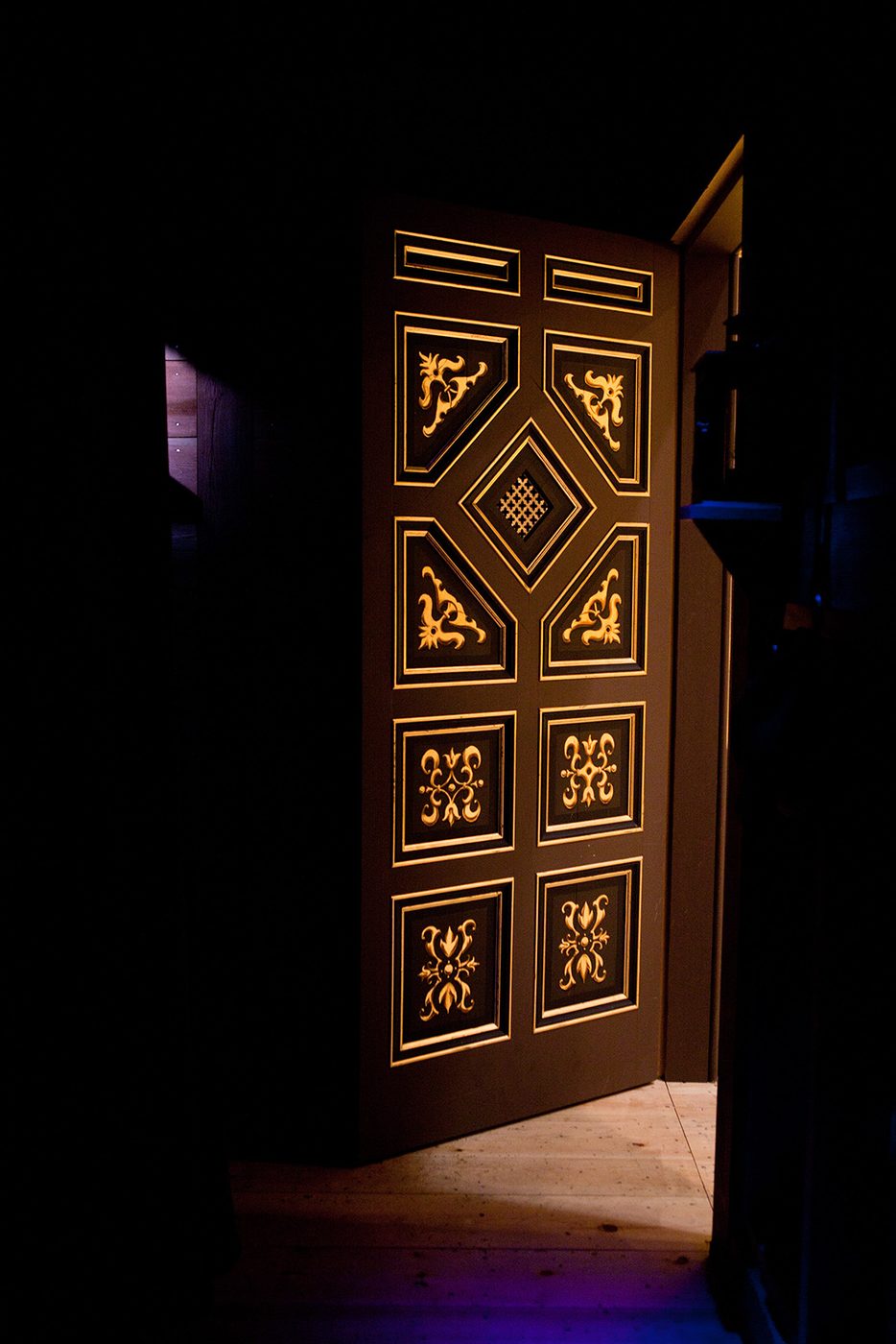 A painted panelled door stands ajar, with sable and gold detailing.