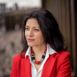 Professor Farah Karim-Cooper wearing a red blazer, white shirt and colourful necklace.