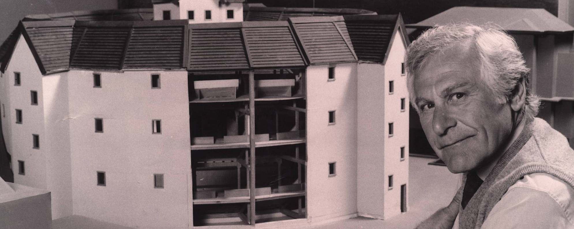 A man sits before a model box of a circular timber structure theatre